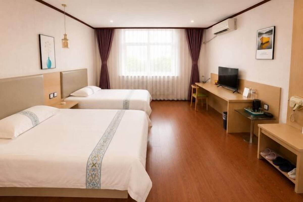 Een hotelkamer met twee bedden, een bureau, een televisie en een raam met gordijnen.