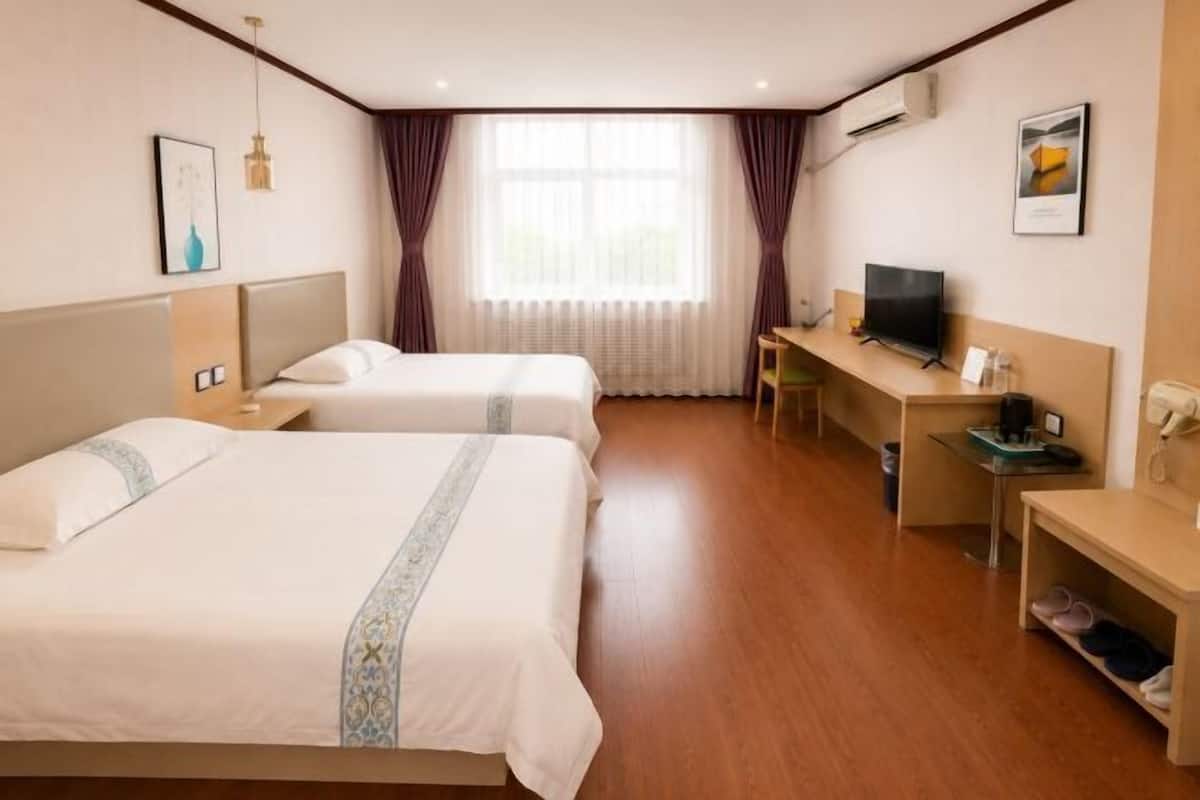 A hotel room with two beds, a desk, a television, and a window with curtains.