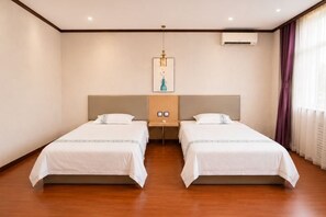 Een hotelkamer met twee bedden, een houten vloer, een nachtkastje met een lamp en een wandairconditioner.