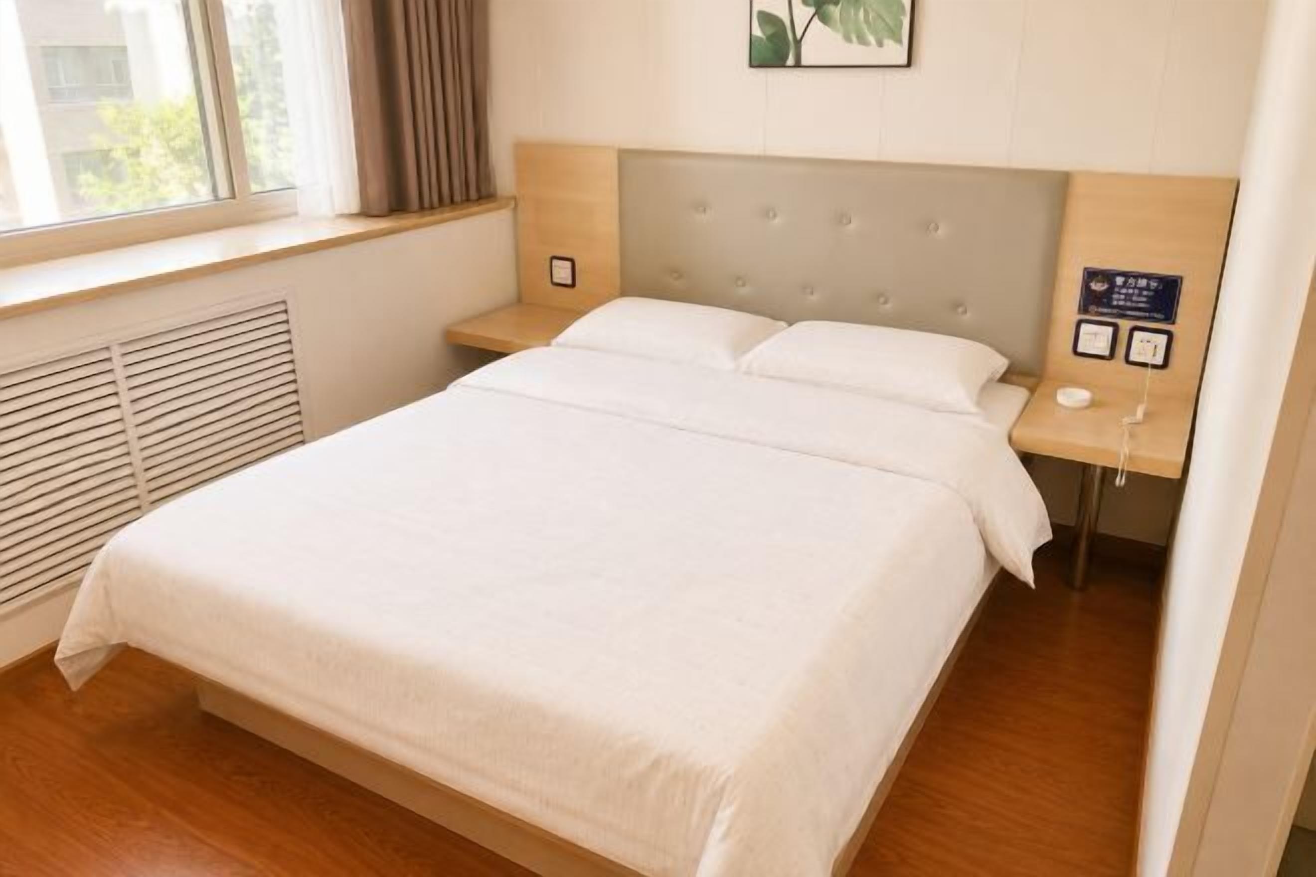 A hotel room with a large bed, a headboard, a bedside table, a nightstand, and a window with curtains.