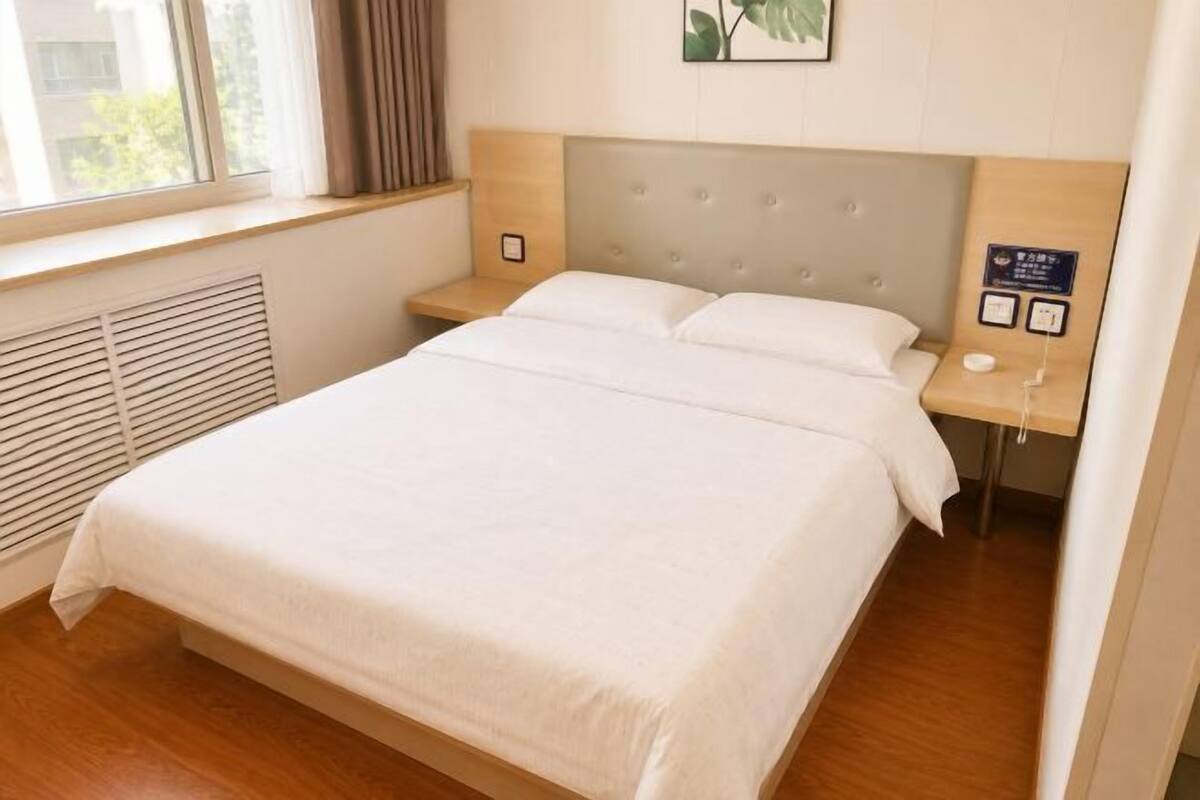 Een hotelkamer met een groot bed, een hoofdeinde, een nachtkastje en een raam met gordijnen.