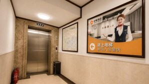 Un pasillo de hotel con un ascensor, un extintor, un mapa enmarcado y un cartel en la pared.