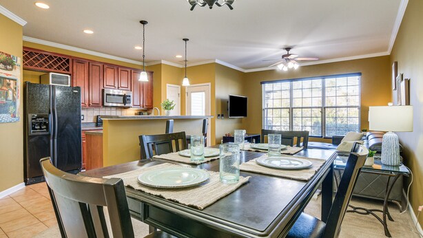 A dining area with a table set for four, surrounded by chairs, in a kitchen with wooden cabinets and a built-in microwave. - Spacious Retreat Near RDU ~ Pool, BBQ, Fast Wi-Fi & Easy Self Check-In (Morrisville)