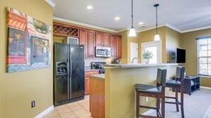 A kitchen with wooden cabinets, a stainless steel refrigerator, a microwave, and a bar area with two stools. - Spacious Retreat Near RDU ~ Pool, BBQ, Fast Wi-Fi & Easy Self Check-In (Morrisville)