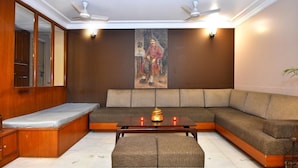 A modern living room with a sectional sofa, a small table with candles, and a painting on the wall. - Pink Cozzy (Jaipur)