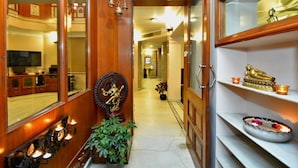 A hallway with wooden doors, a statue, a potted plant, and a shelf with decorative items. - Pink Cozzy (Jaipur)