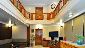 A spacious living room with a high ceiling, a wooden staircase, a flat-screen TV, and a potted plant. - Pink Cozzy (Jaipur)