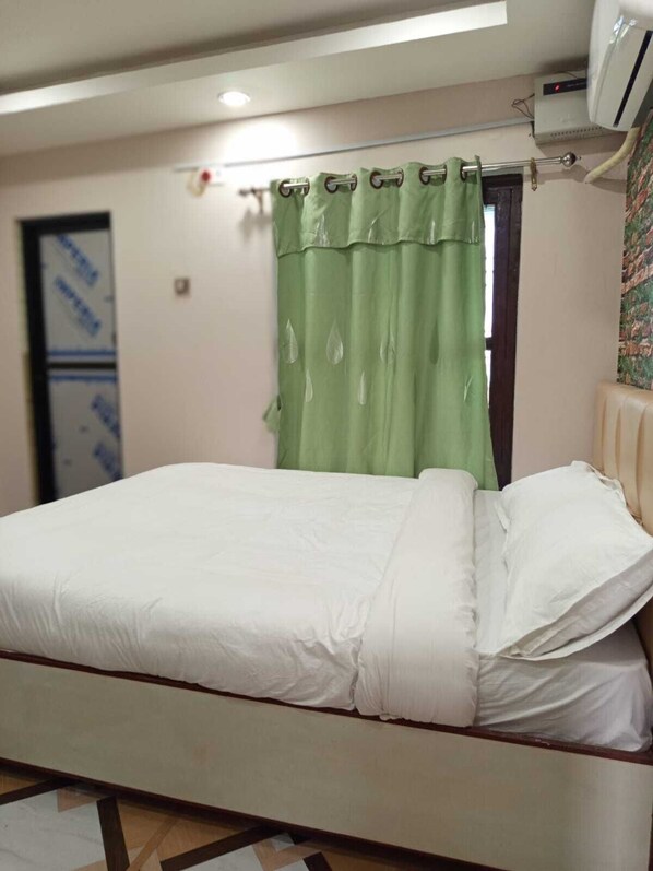 A bed with white bedding, a green curtain, and an air conditioning unit on the wall.