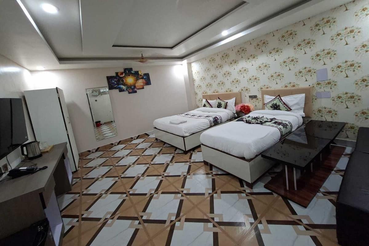 A hotel room with two beds, a desk, a TV, and a patterned floor.
