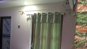 A bedroom with a bed, green curtains, a ceiling fan, and an air conditioning unit. - HOTEL DEV INN (Dhangadhi)