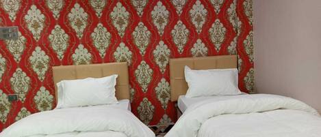 A hotel room with two beds, a red patterned wallpaper, an air conditioner, and a power outlet on the wall.