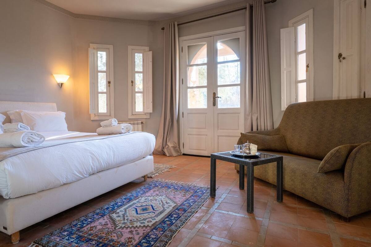 A bedroom with a bed, a chair, a small table, and a patterned rug.