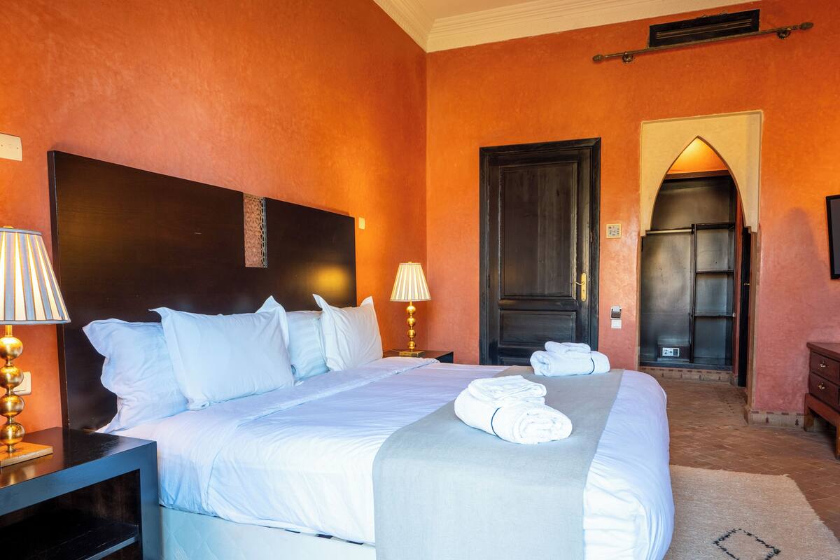 A hotel room with a large bed, two bedside lamps, a TV, and a door leading to another room.