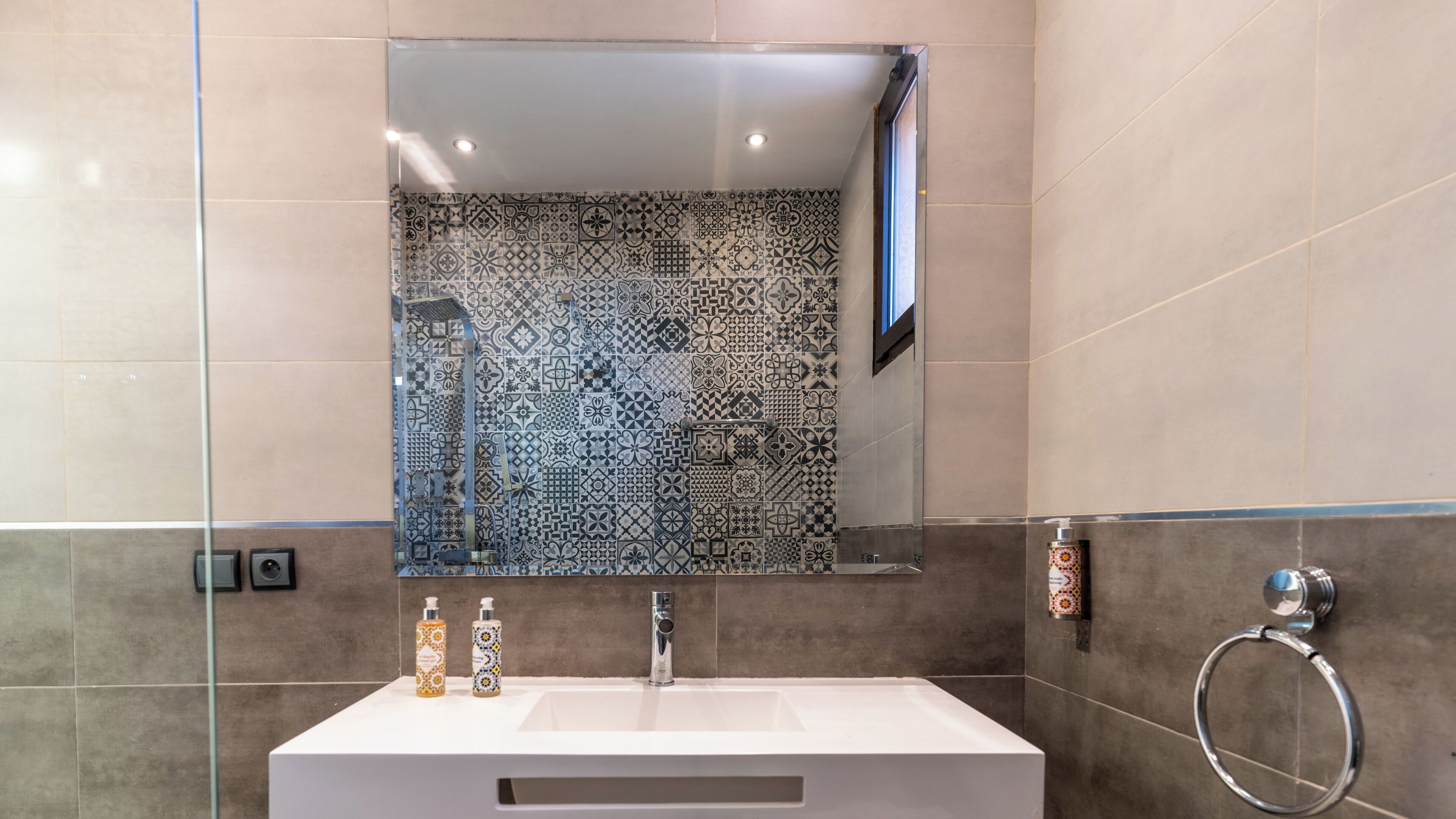 Une salle de bain avec un mur carrelé, un miroir, un lavabo et deux flacons de produits de toilette.