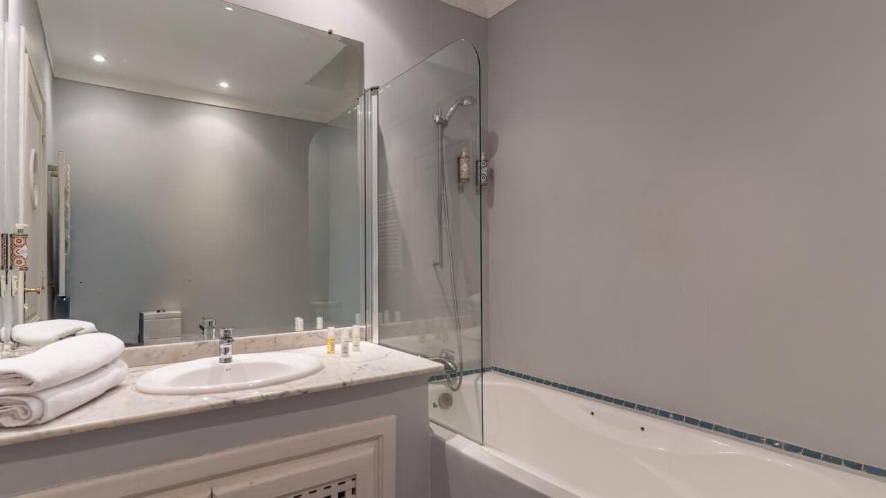 Een moderne badkamer met een douche met glazen wand, een wastafel met een marmeren blad en een grote spiegel.
