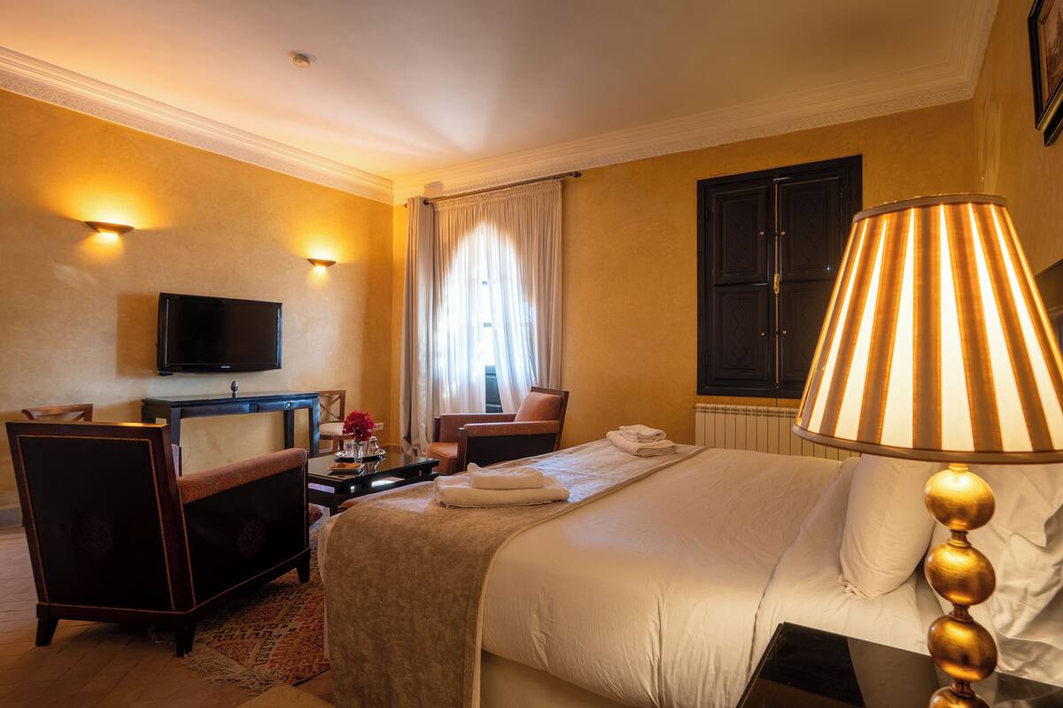 A hotel room with a bed, a desk, a chair, a television, and a lamp.