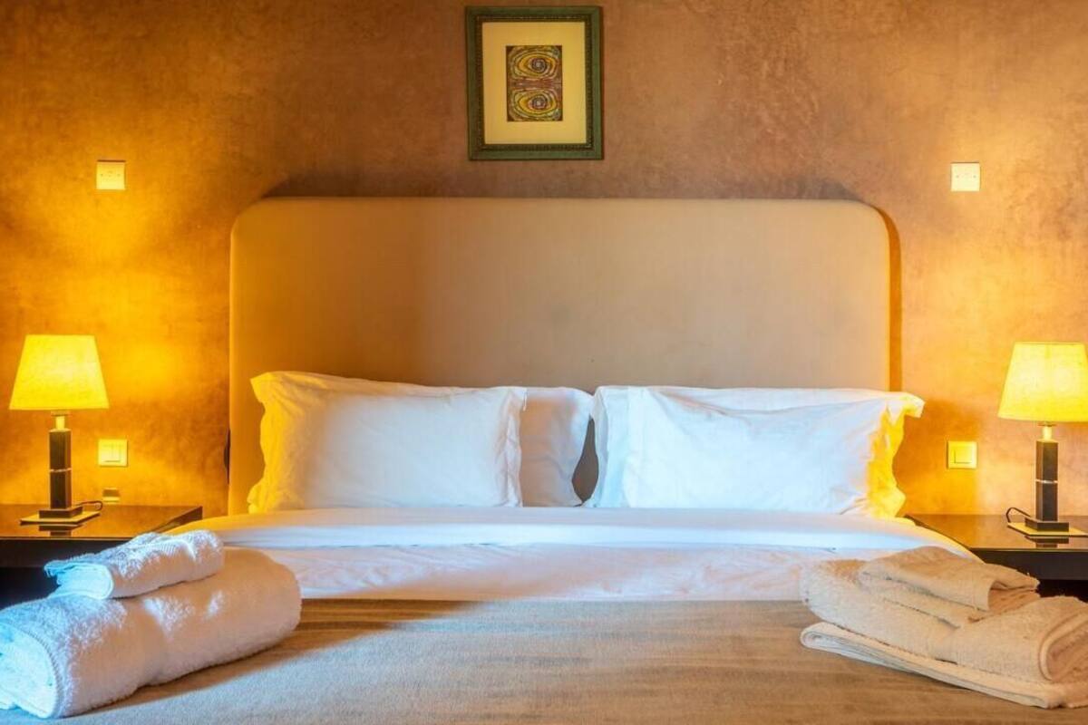 A hotel room with a bed, two bedside lamps, and a framed picture on the wall.