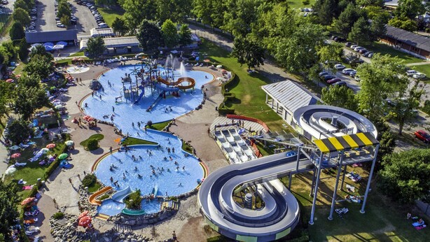 Luchtbeeld van een waterpark met meerdere glijbanen en zwembaden, omringd door picknickplaatsen en bomen.