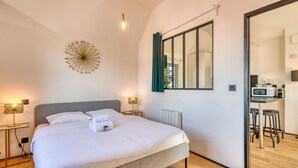 Ein modernes Schlafzimmer mit einem großen Bett, Nachttischlampen, einer dekorativen Deckenleuchte und Blick in einen Küchenbereich.