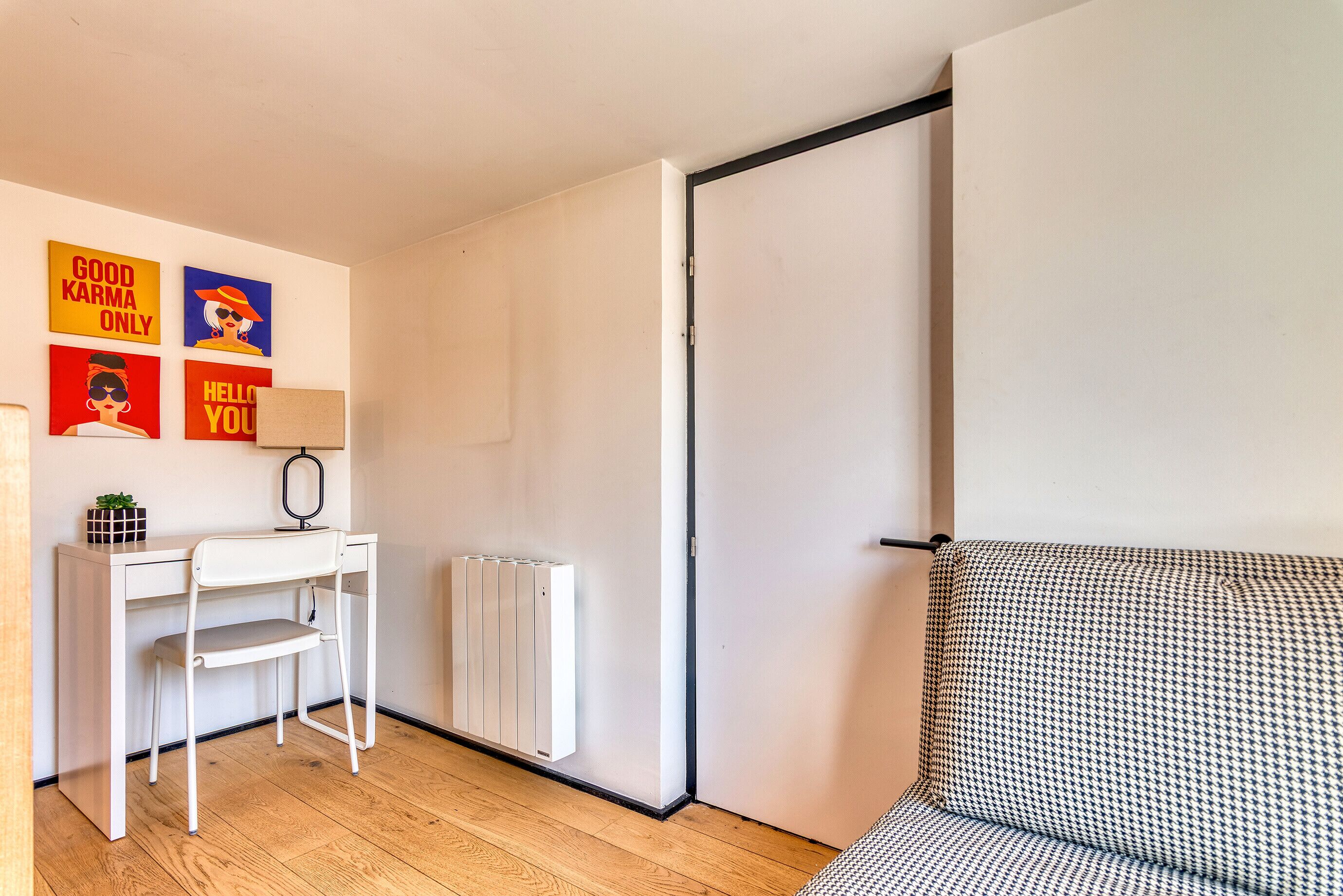 Une pièce avec un bureau blanc, un canapé à motifs pied-de-poule, un radiateur et des affiches motivantes accrochées au mur.