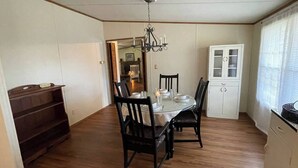 Ein Essbereich mit einem runden Tisch, schwarzen Stühlen, einer Chandelüster, einem weißen Schrank und einem Holzbodenregal.