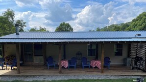 Eine Hütte mit verdeckter Veranda, blauen Adirondack-Stühlen und einer rot-weißen Karotischdecke.