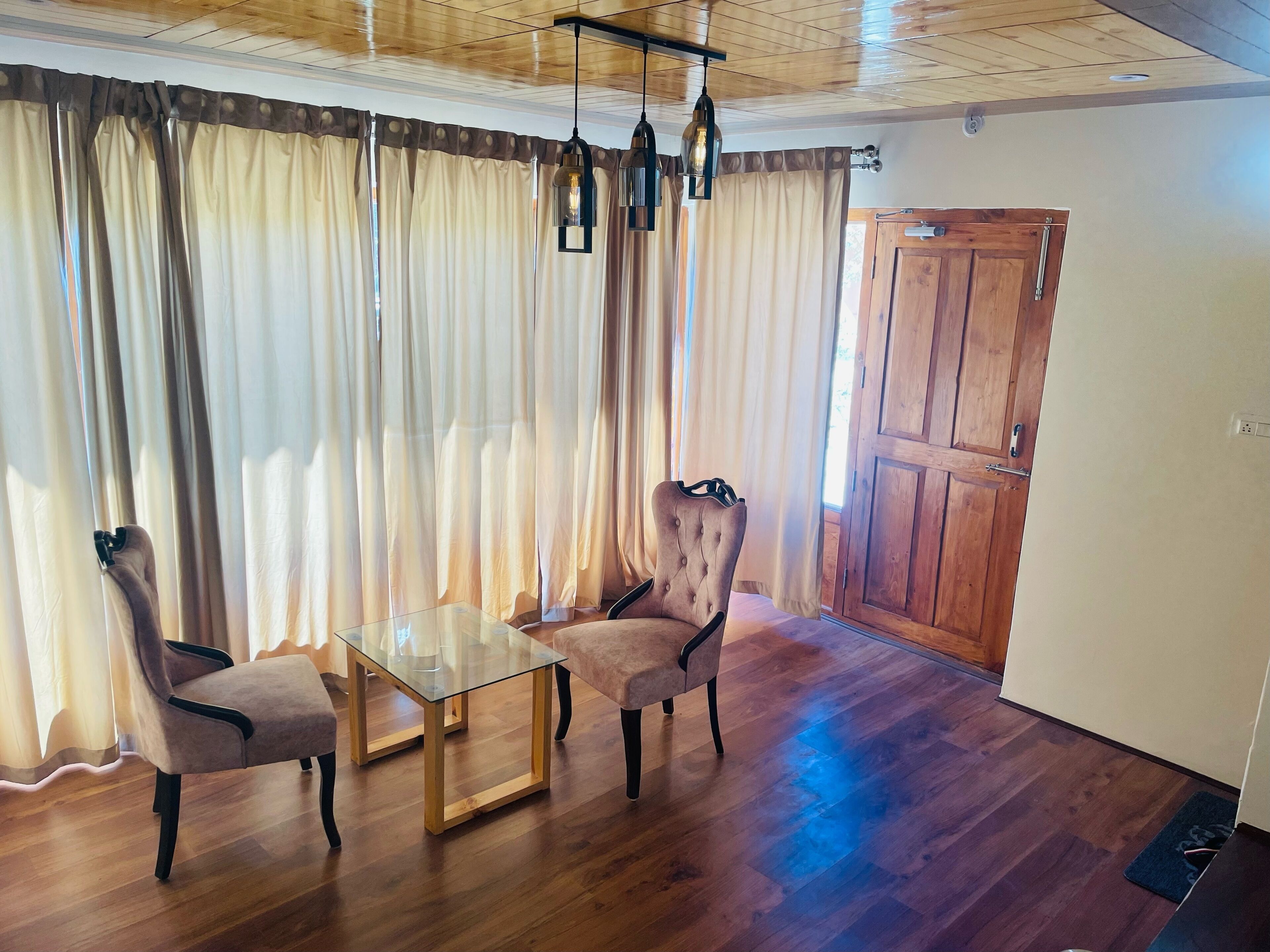 Ein Zimmer mit Holzboden, einem Glastisch, zwei Polsterstühlen und einer Holztür.