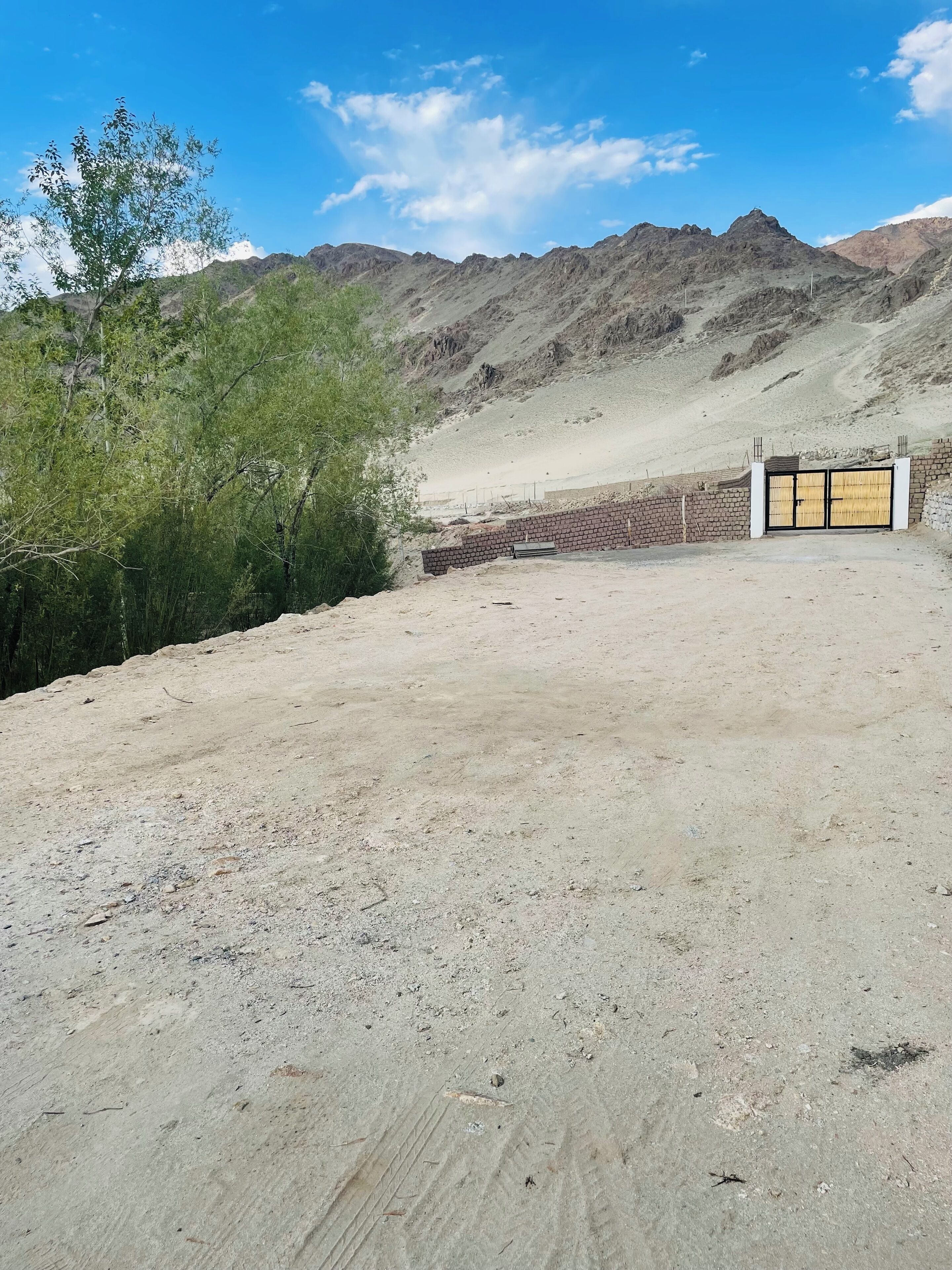 A desert landscape with a paved area, a brick wall, and a gate.