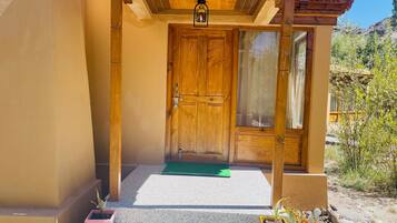 A wooden door with a glass panel, a wooden porch with a green mat, and potted plants on the steps.