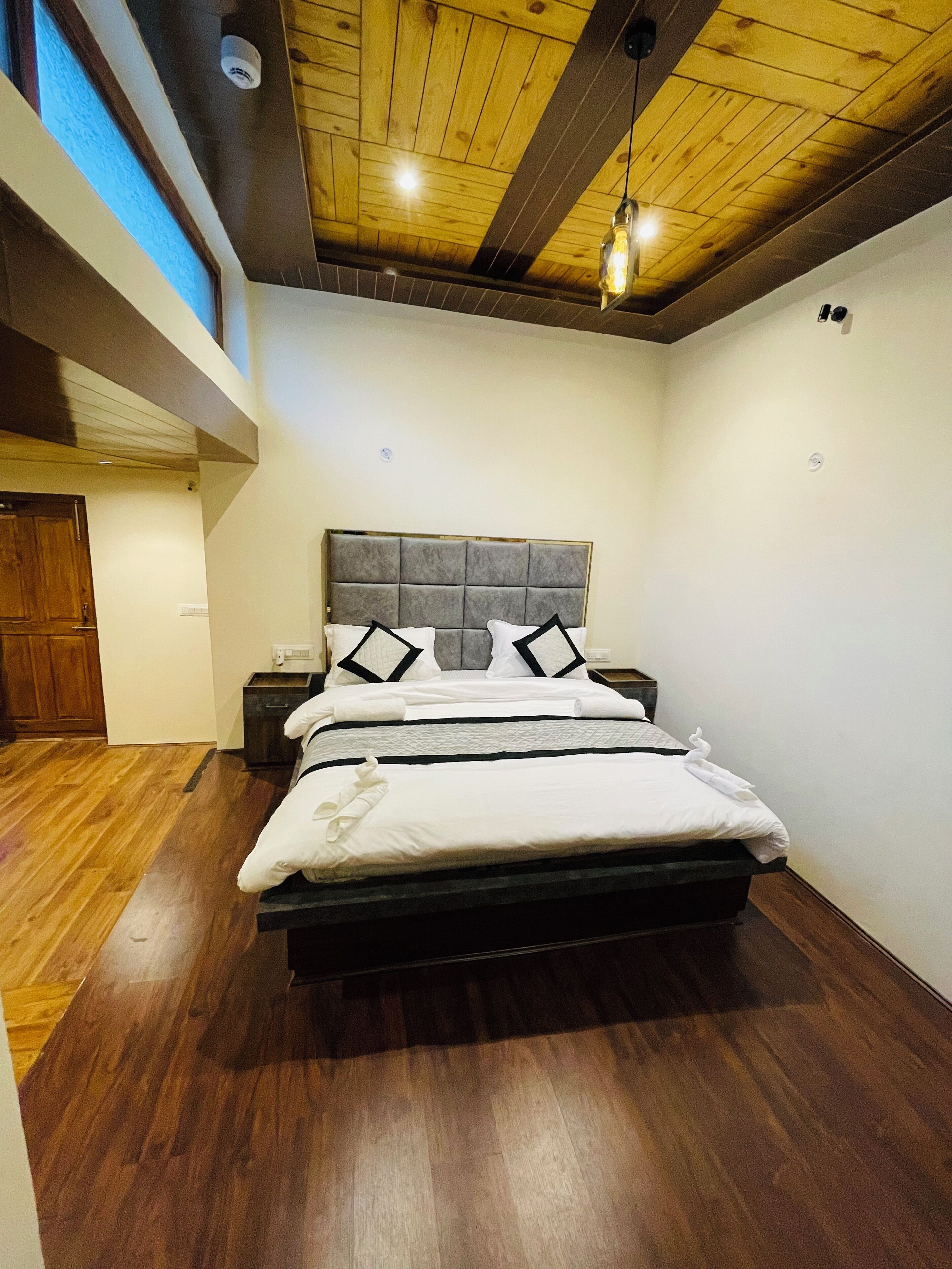 Une chambre à coucher moderne avec un plafond en bois, un grand lit doté d’une tête de lit grise et un plancher en bois.