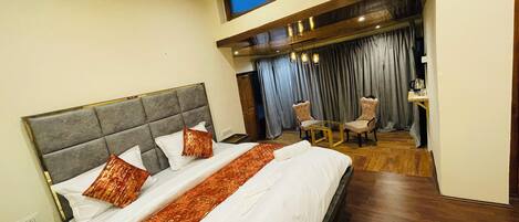 A hotel room with a large bed, a small table with chairs, and a view of the sky through a window.
