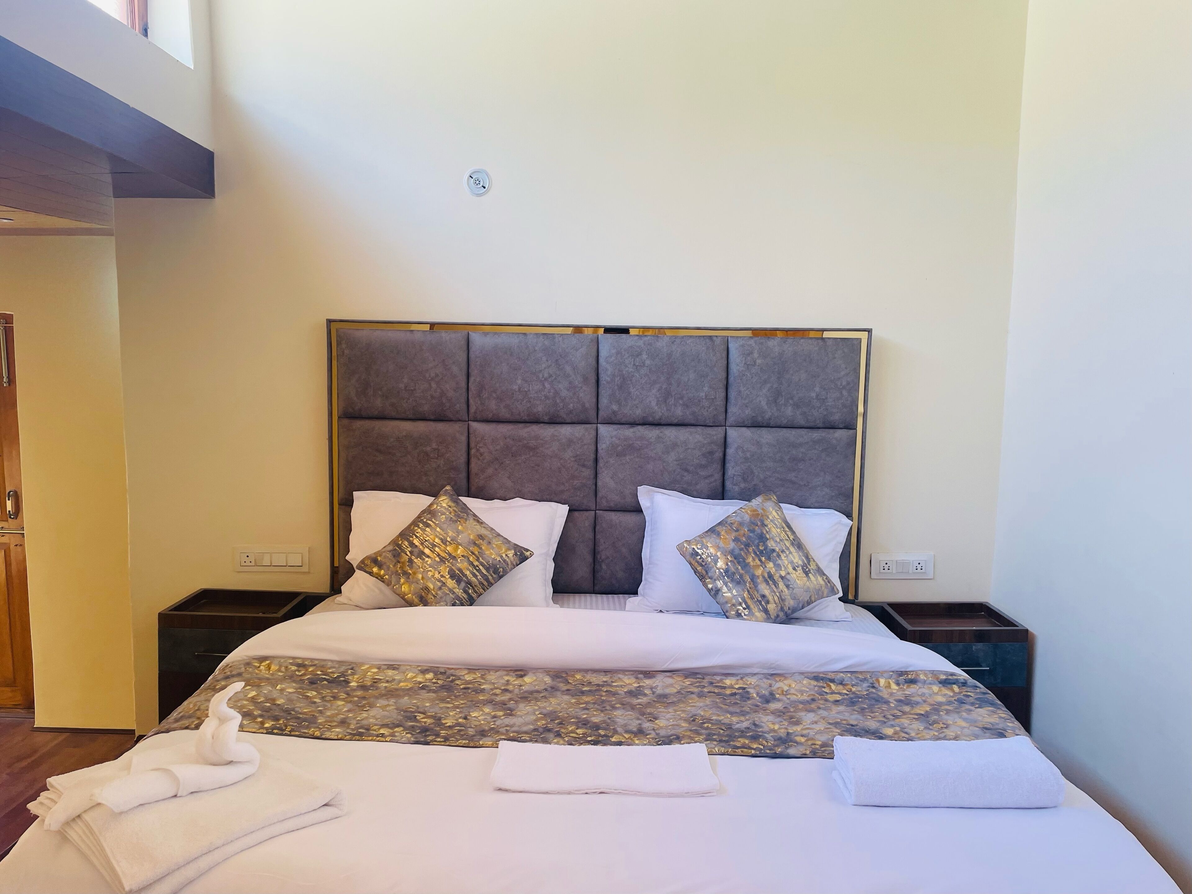 Una cama bien hecha con un cabecero capitonado, dos almohadas decorativas y una colcha con estampado floral.