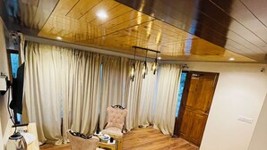 A spacious room with a wooden floor, a large window with curtains, a sofa, a chair, and a small table with a kettle. - Thiksay Organic Resort and Retreat (Leh)