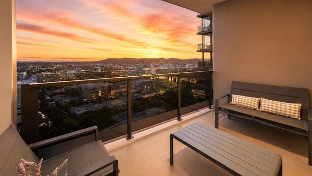 A balcony with a city view at sunset, a bench, and a table. - Sky-High 2BR|Spectacular Views|Free Parking! (South Brisbane)