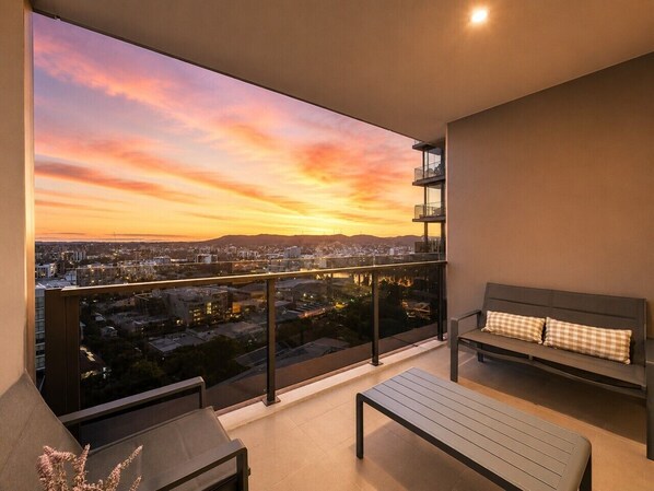 A balcony with a city view at sunset, a bench, and a table.