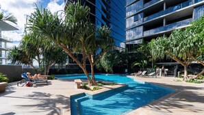 A swimming pool with lounge chairs, surrounded by palm trees and a modern building. - Sky-High 2BR|Spectacular Views|Free Parking! (South Brisbane)