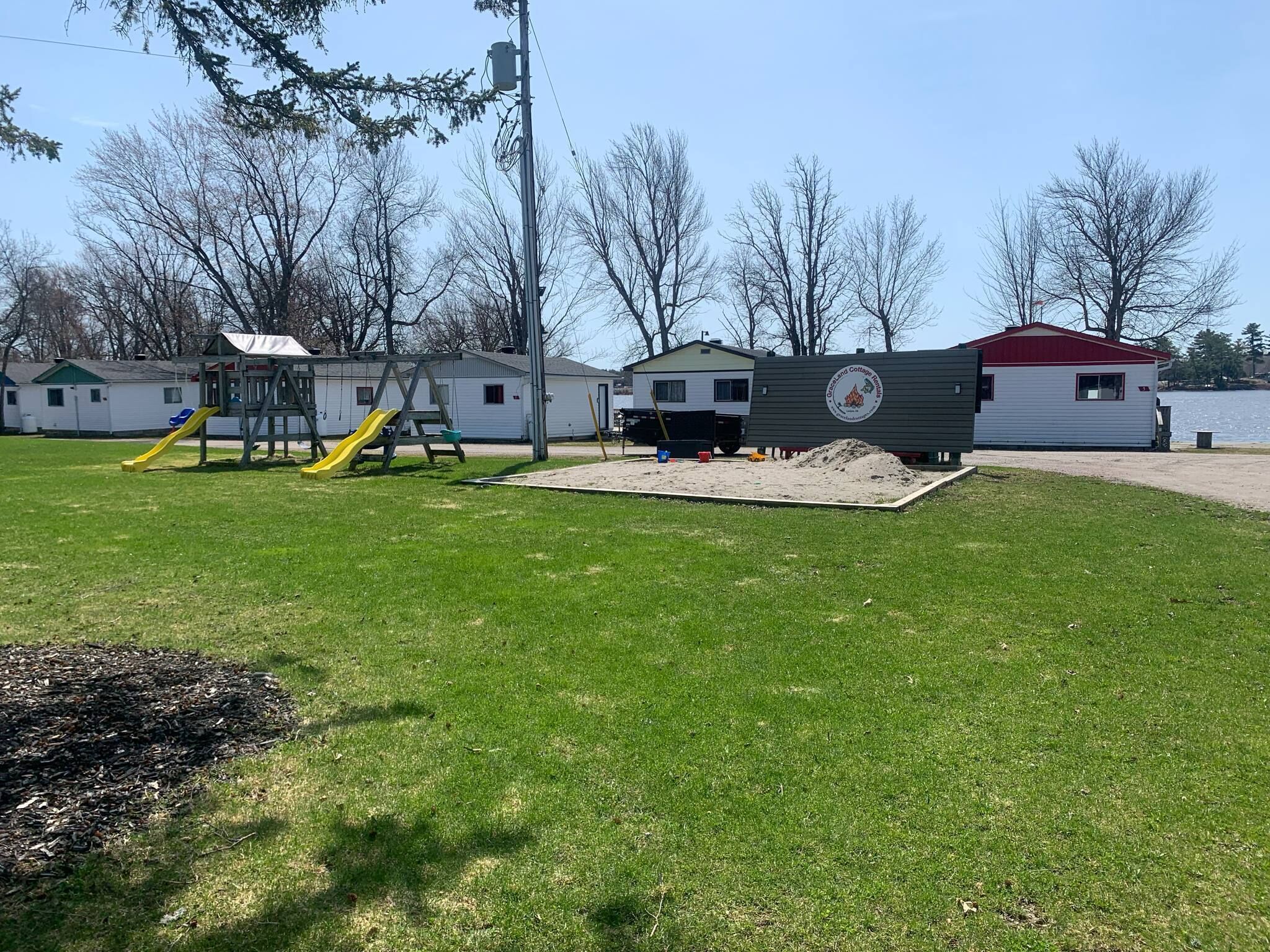 A playground with slides and a sandpit, surrounded by a grassy area and a body of water.
