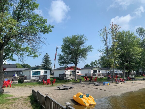 A lakeside campsite with cabins, a sandy beach, and a yellow inflatable raft.