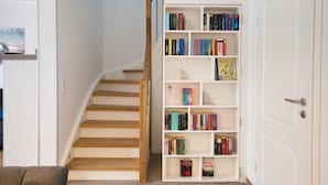 Eine Treppe führt zu einem Raum mit einer weißen Tür, einem Bücherregal voller Bücher und einem braunen Sofa.
