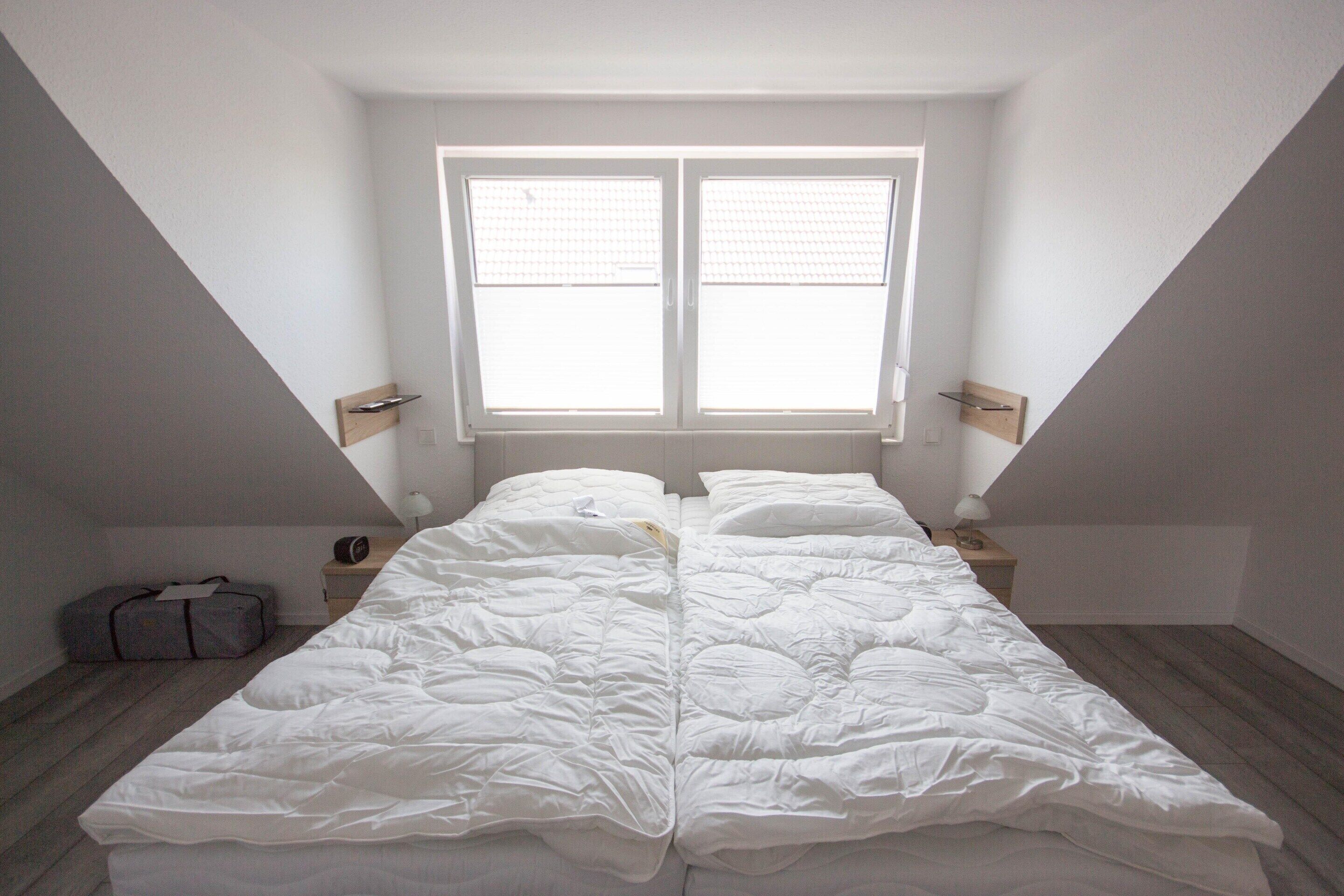 Une chambre avec un grand lit, une fenêtre et une valise posée sur le sol.