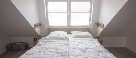 Une chambre avec un grand lit, une fenêtre et une valise posée sur le sol.