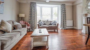 A living room with a sofa, armchair, and coffee table, large windows with curtains, and a radiator. - Brook House - UK43013 (Berkeley)
