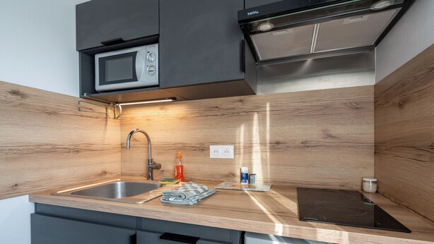 A modern kitchen with a wooden backsplash, stainless steel appliances, and a built-in induction cooktop. - Le Rivage - Wifi - Centre-ville (Le Mans)