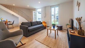 Una sala de estar moderna con un sofá gris, una mesa de centro de madera y una escalera que lleva a un nivel superior.