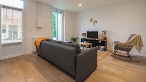 Una sala de estar moderna con un sofá gris, un sillón mecedora, un televisor y una mesita con una planta.