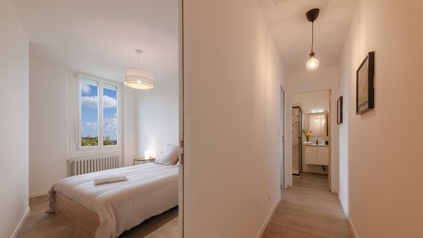 Un dormitorio con una cama grande, una ventana, un radiador, una mesita de noche y una lámpara colgante.