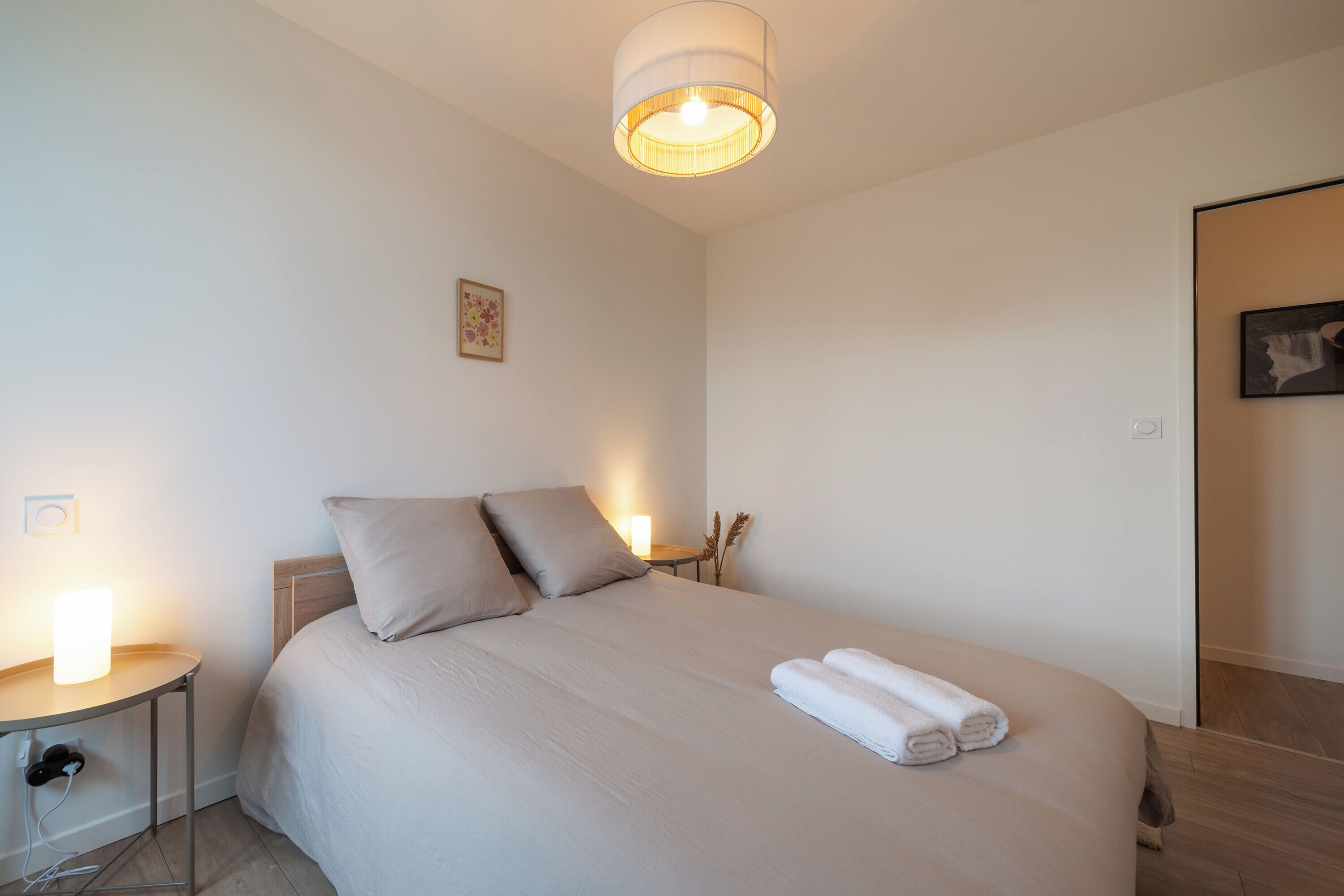 A neatly made bed with pillows, a bedside lamp, and a wall-mounted light fixture in a clean, minimalistic room.