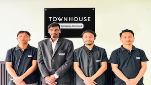 Quatre personnes se tiennent devant un panneau sur lequel on peut lire : « TOWNHOUSE, services d’entretien fournis par l’entreprise ».