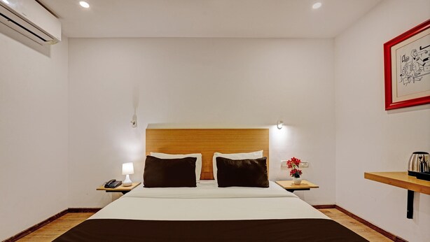 Une chambre d’hôtel avec un grand lit, une tête de lit en bois, une table de chevet avec une lampe, un téléphone et une petite table sur laquelle est posé un vase de fleurs.
