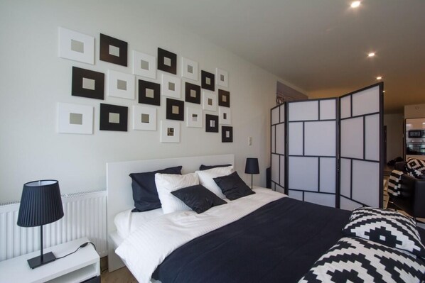 A modern hotel room with a neatly arranged bed, a bedside table with a lamp, and a wall decorated with square picture frames.